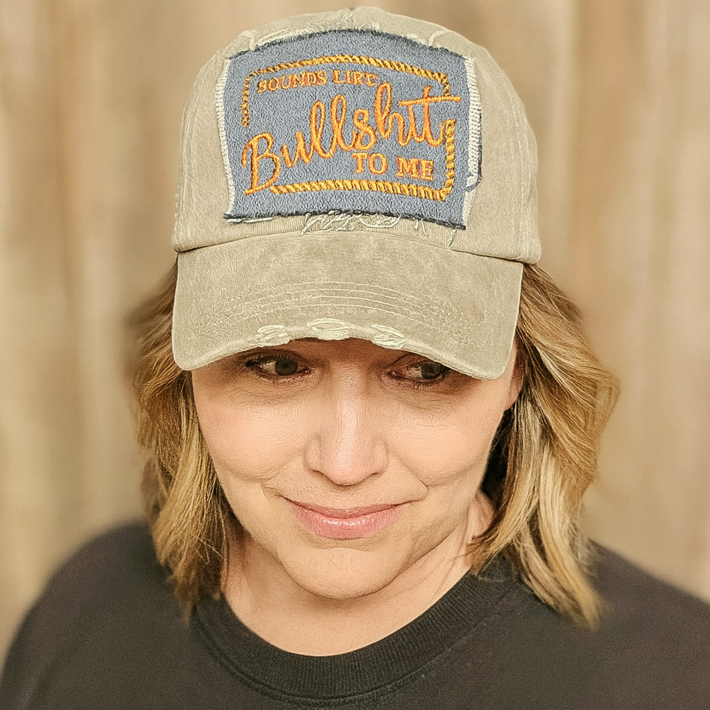 Person wearing a cap with a patch that reads 'SOUNDS LIKE BULLSHIT TO ME' against a beige background