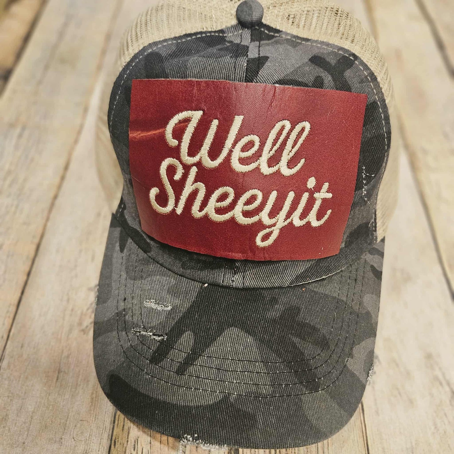 Camouflage baseball cap with a red patch embroidered with "well sheeyit", grey camo adjustable ponytail cap