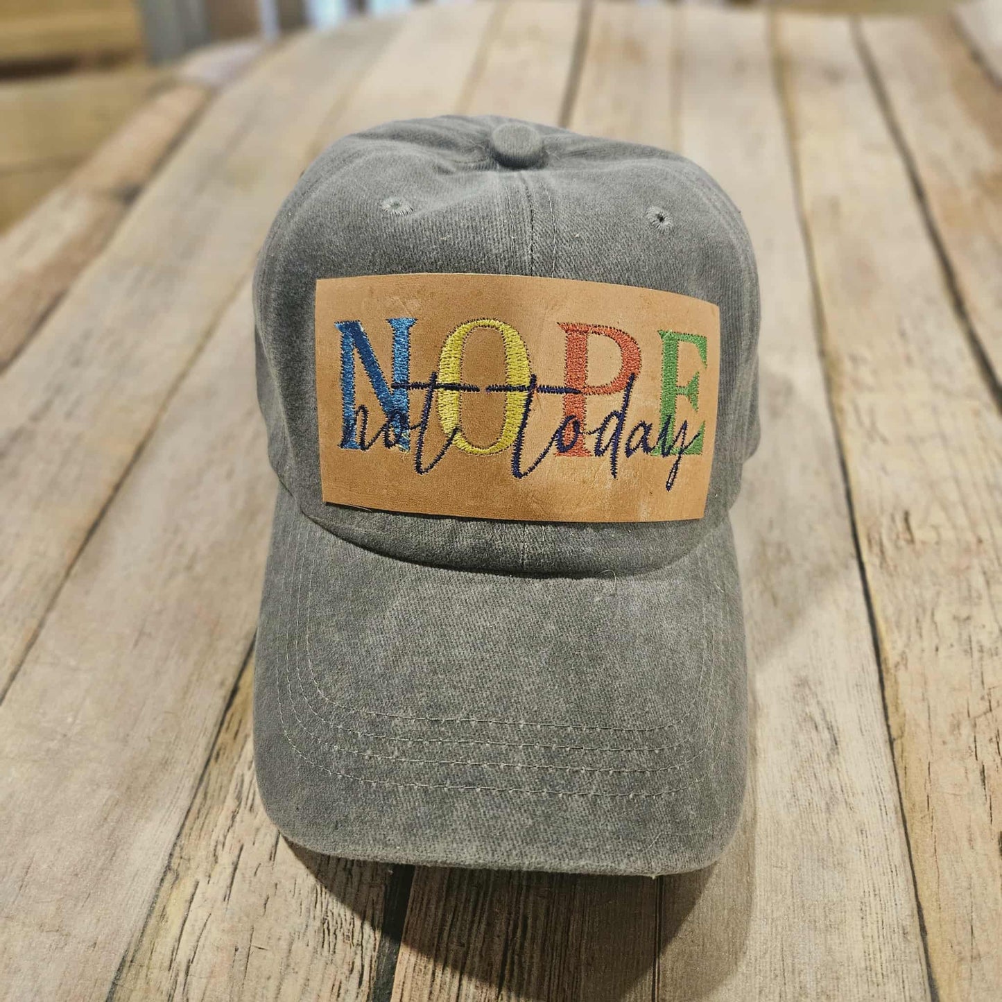 Gray cap with a colorful 'NOPE not today' patch on a wooden surface