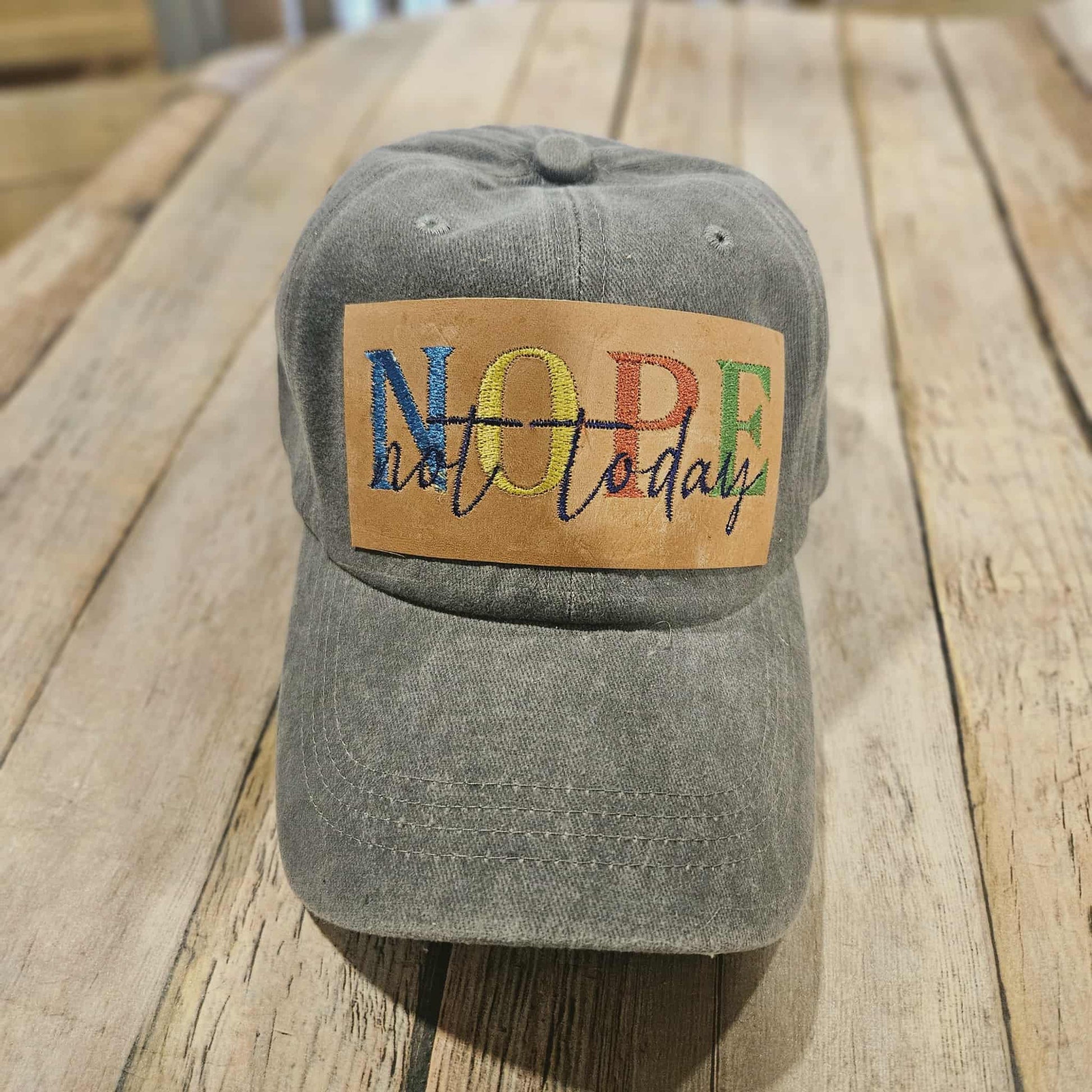 Gray cap with a colorful 'NOPE not today' patch on a wooden surface