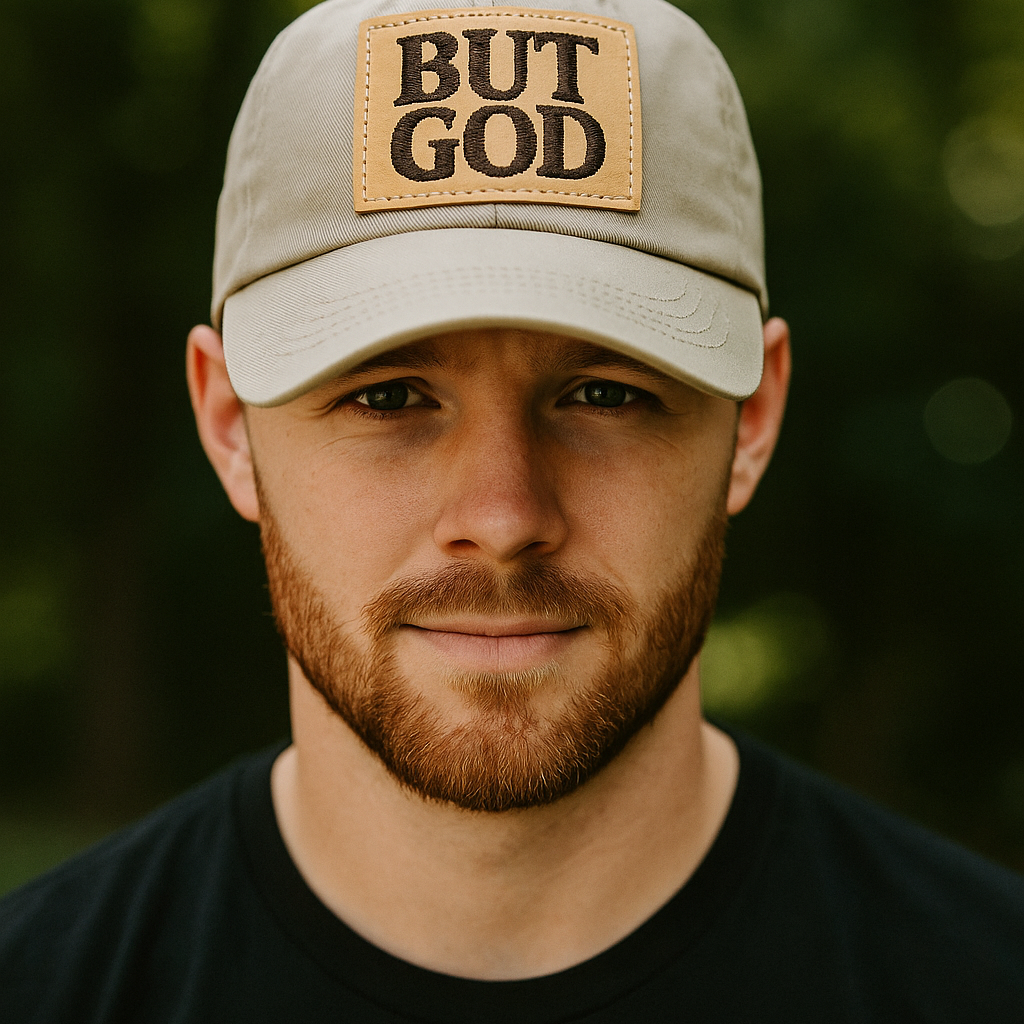 Man wearing a beige cap with 'BUT GOD' text against a blurred green background