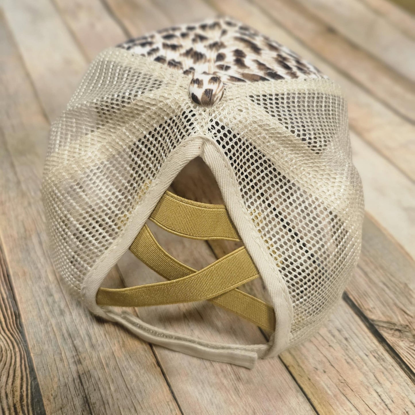 Beige mesh cap with leopard print visor on a wooden surface